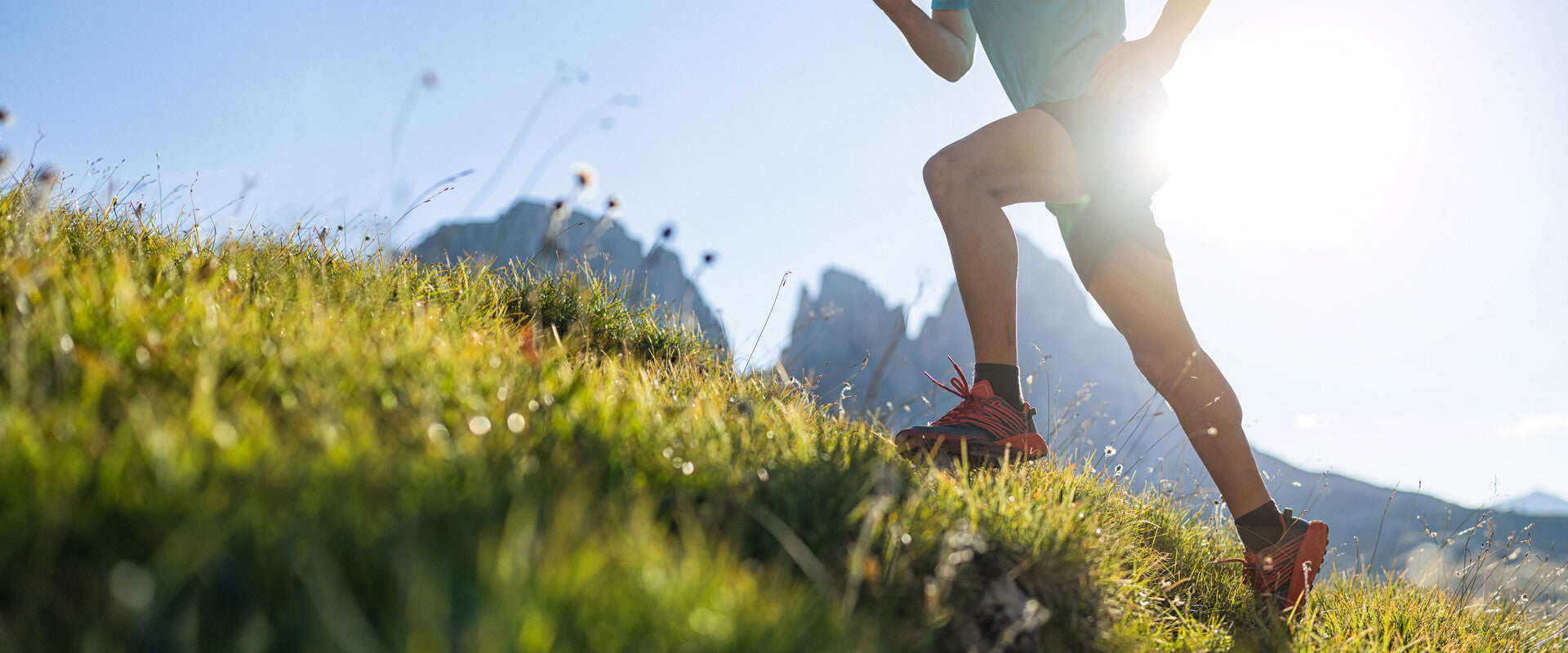 Ein Sportler, der über grüne Bergwiesen läuft, bei sehr sonnigem Wetter